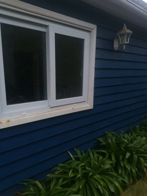 Ventana corredera de PVC blanca en casa de madera azul